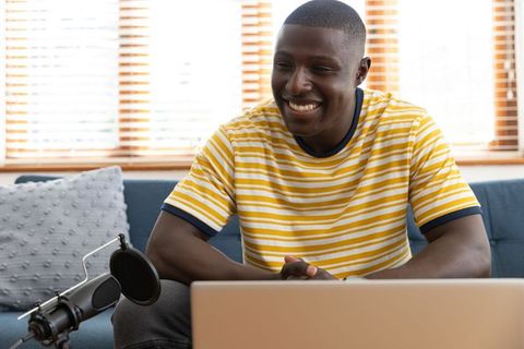 Content creator smiling in home studio with microphone and laptop