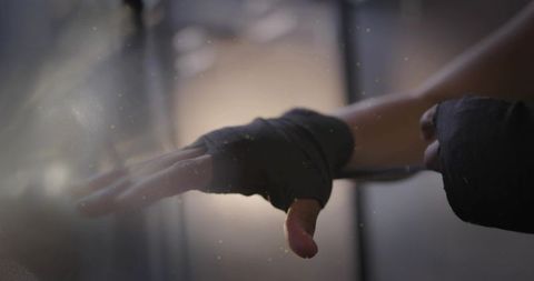 Mid-adult woman wrapping hands before boxing training in backlit gym with dust and chalk