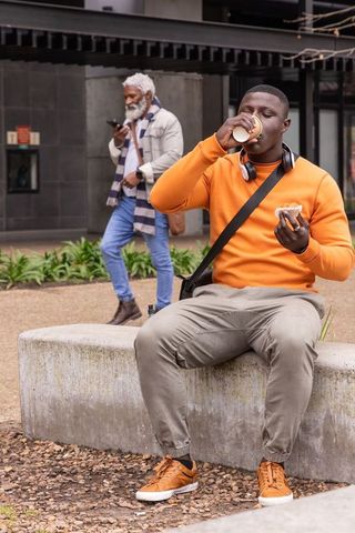 Urban plaza coffee break: young african american man sipping coffee while eating pastry