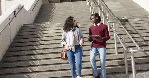 Young friends walking down urban stairs discussing ideas on tablet, casual campus scene