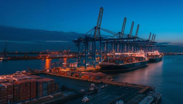 Gantry cranes loading containers at twilight port terminal with illuminated cargo ship