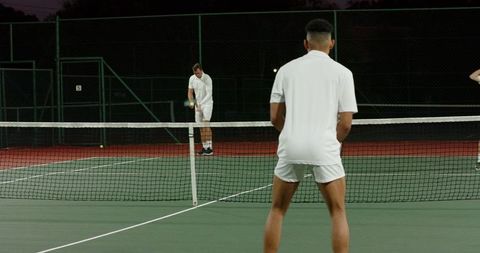 Diverse players preparing serve on outdoor night hardcourt wearing white tennis attire
