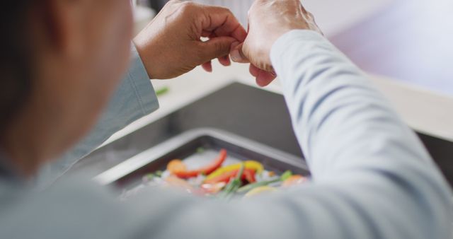 Close-up view of an individual preparing fresh vegetables in a modern kitchen. Perfect for illustrating healthy eating habits, culinary arts, cooking tutorials, or lifestyle articles focused on home cooking and nutrition.