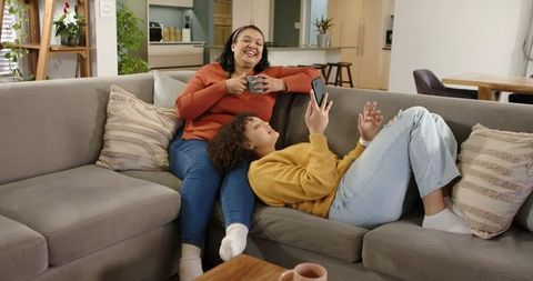 African American mother and daughter laughing and relaxing on gray sectional sofa at home