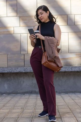 Young professional checking smartphone while holding coffee on urban plaza