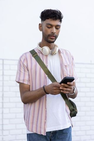 Indian man using smartphone on rooftop wearing headphones pink striped shirt