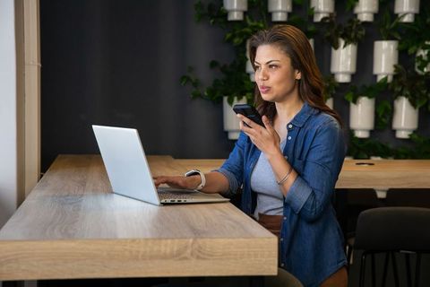 Woman using laptop and speaking into smartphone in modern coworking space