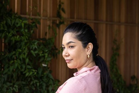 Confident woman turning on patio with wooden paneling, climbing ivy and pink top