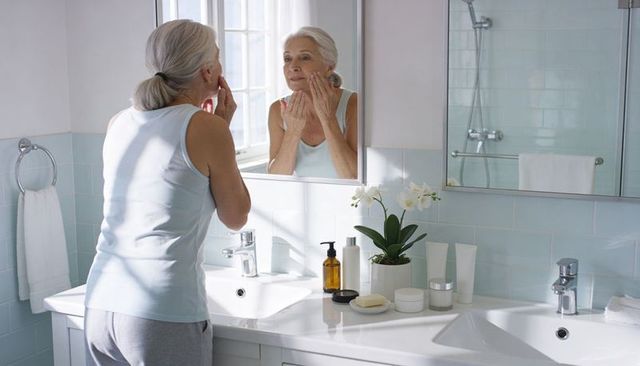 Senior woman applying skincare at double-sink vanity morning routine mirror reflection