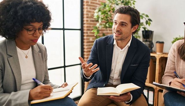 Discussing ideas in modern office nook with gesturing colleague and note-taking teammates