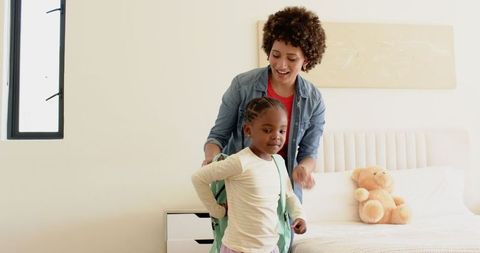 Mother Helping Young Daughter with Backpack in Bedroom