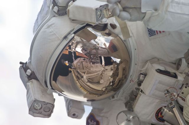 This image captures an astronaut conducting a spacewalk, with the Space Shuttle Discovery's cargo bay visible reflected in the helmet visor. It originates from mission STS-105. Useful for articles about space exploration, NASA missions, astronaut training, technology in space, or highlighting human achievement in space.