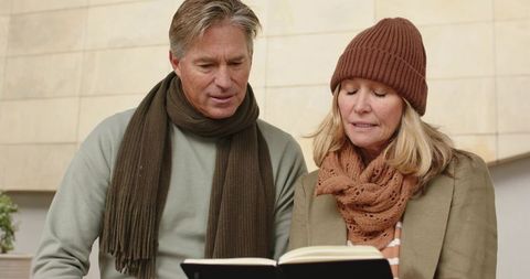 Mature couple reading book wearing scarves and beanie, cozy autumn warmth and togetherness