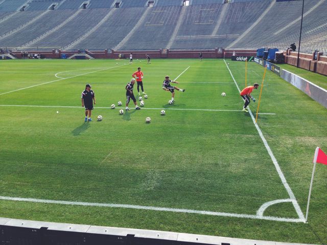 This depicts soccer players training on a professional field with a coach overseeing the session. It demonstrates teamwork, dedication, and athletic skills. Ideal for use in sports-related content, training manuals, promotional material for soccer academies, or articles about soccer training and youth sports development.