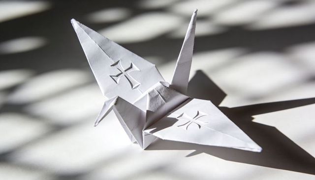 White origami crane casting sharp shadow with blinds light pattern minimalist geometry cutout