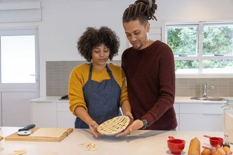 Couple baking lattice pie together in bright modern kitchen with window and countertop