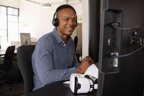 African American man wearing headphones participating in virtual meeting with VR headset