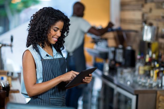 Waitress with curly hair using a digital tablet in a cafe, smiling while working. Ideal for illustrating modern technology in the hospitality industry, customer service, and efficient restaurant management. Suitable for articles, blogs, and advertisements related to cafes, restaurants, and digital solutions in service industries.