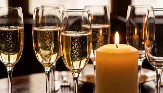 Sparkling champagne flutes surrounding glowing pillar candle on intimate dining table