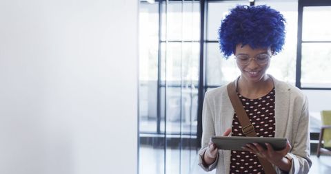 Confident businesswoman with blue afro using tablet in modern office