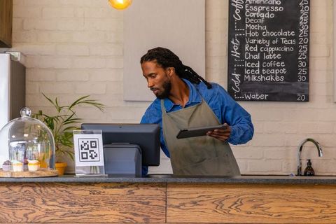 African-american barista using tablet at rustic coffee counter with pastries