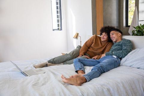 Happy couple relaxing on bed with laptop in cozy bedroom setting