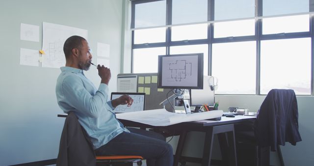 Architect reviewing blueprints on a well-organized modern office desk with computer and notes. Ideal for use in themes relating to architecture, engineering, design projects, technical work, professional environments, creative processes, and modern workspaces.