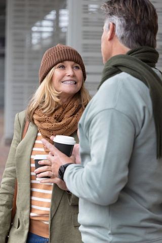 Middle-aged couple smiling and chatting while holding takeaway coffee outside shuttered storefront