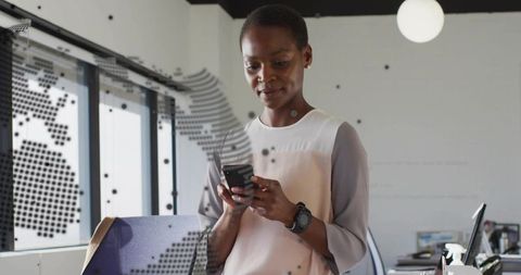 Professional woman checking smartphone in bright modern office wearing layered blouse