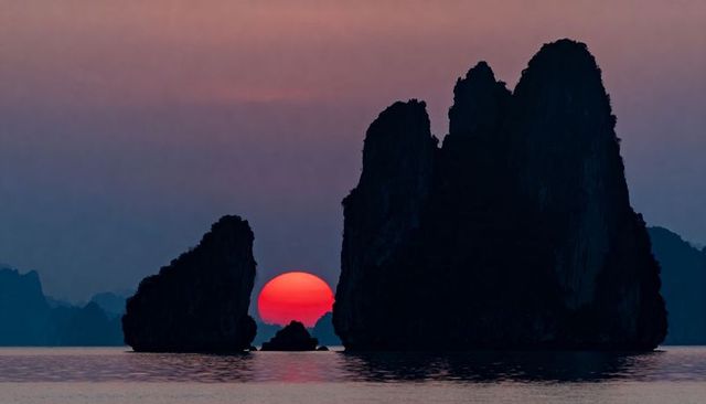 Sun sinking between karst islets creating deep silhouette and reflective sea