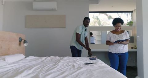 African american couple packing luggage in minimalist room, woman holding tablet