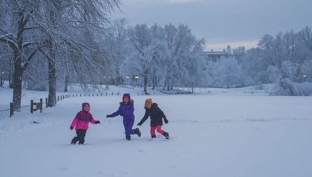 Running children crossing snowy park at dusk with frosted trees lampposts and footprints