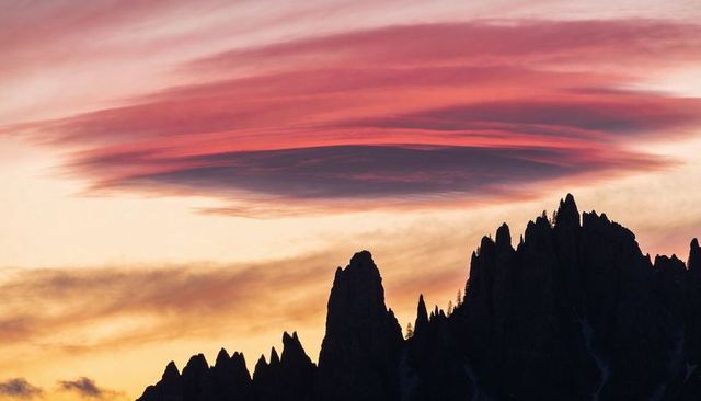 Lenticular cloud hovering over jagged alpine ridge silhouetting peaks at dusk