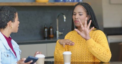 African american friends chatting over coffee at kitchen counter wearing yellow sweater