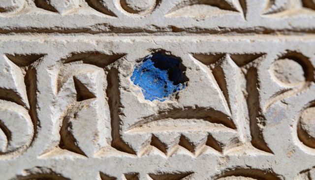 Weathered stone carving with bright blue pigment accent, macro textured relief detail