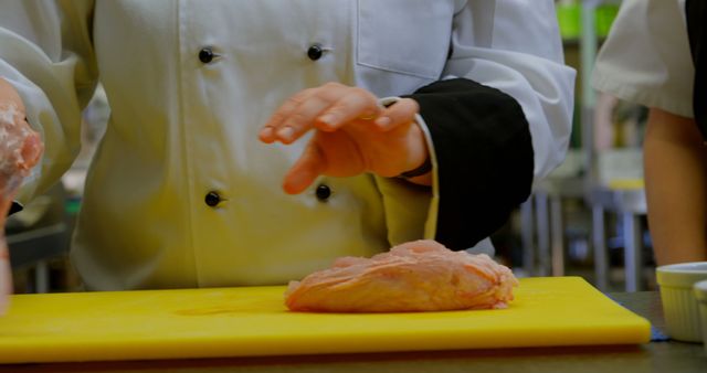 A chef is preparing chicken on a yellow cutting board, with copy space. Their professional attire suggests a focus on culinary skills and food safety in a kitchen environment.