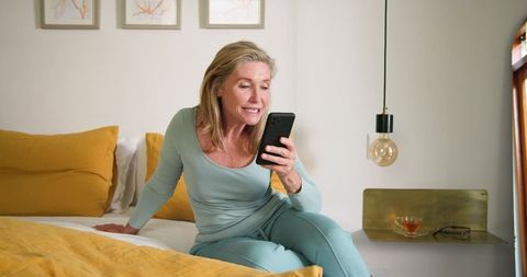 Senior Woman in Teal Loungewear Using Smartphone for Relaxation at Home
