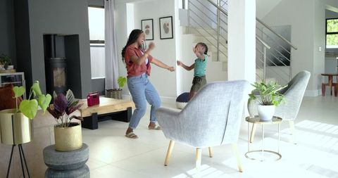 African mother and daughter dancing at home with red speaker in sunlit modern living room