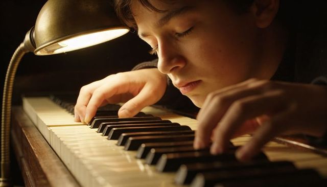 Teen practicing piano by lamplight showing focused expression and gentle hands