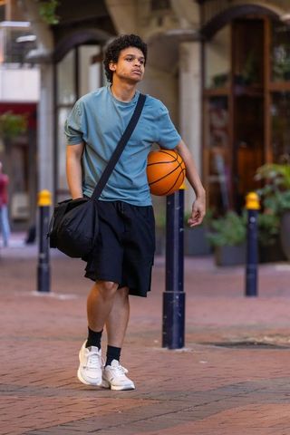 African american young man walking with basketball and duffel bag in urban plaza wearing sneakers