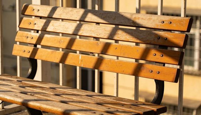 Weathered wooden bench bathed in golden sunlight on urban balcony with strong shadows