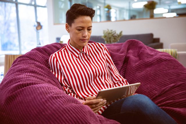 Caucasian businesswoman using tablet in modern office lounge. Ideal for depicting modern work environments, technology in business, and casual professional settings. Useful for articles on remote work, digital transformation, and workplace culture.