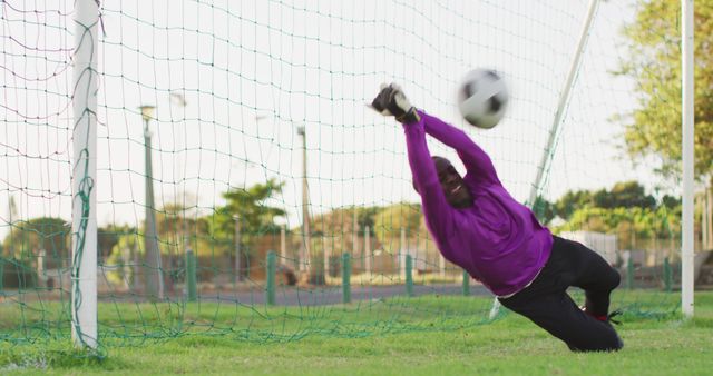 African American goalkeeper making an impressive save in mid-air during a soccer game. Ideal for use in sports event posters, athletic performance promotions, or articles on soccer techniques and training. Action-packed and dynamic scene emphasizing skill, agility, and athleticism.