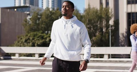 African American man walking confidently on urban rooftop wearing white hoodie