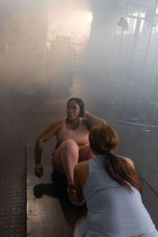 Diverse female fitness partners doing sit-ups in hazy gym with spotter support
