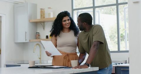 Couple reviewing documents at sunlit modern kitchen island, sharing conversation