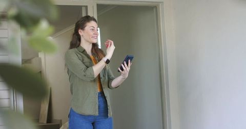 Young woman video calling and gesturing with smartphone and smartwatch in home hallway