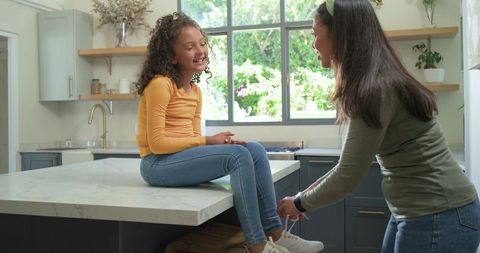 Mother tying daughter sneaker on kitchen island during morning routine
