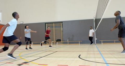 Diverse male friends playing indoor volleyball on gym court showing teamwork and energy