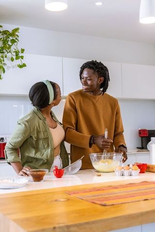 African american couple preparing batter together on kitchen island smiling and connecting